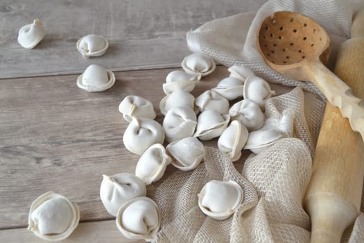 Homemade raw dumplings with flour on a wooden white table.