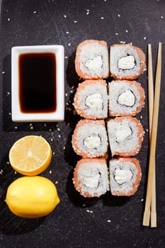 Sushi philadelphia rolls set served with lemon and souce on black board on dark background. Flat layout on black, top view