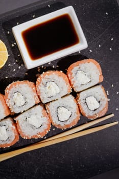 Sushi philadelphia rolls set served with lemon and souce on black board on dark background. Flat layout on black, top view