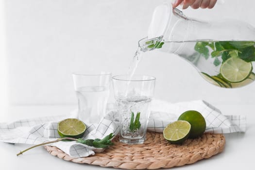 Detox water with lime fruit. Hand pouring lime fruit water from jug into glasses.