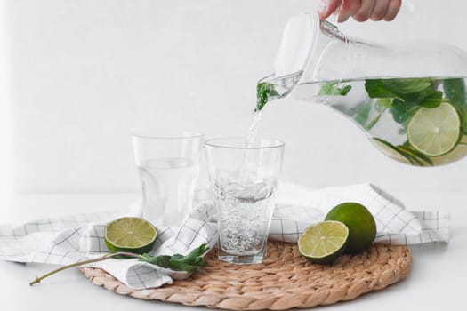 Detox water with lime fruit. Hand pouring lime fruit water from jug into glasses.