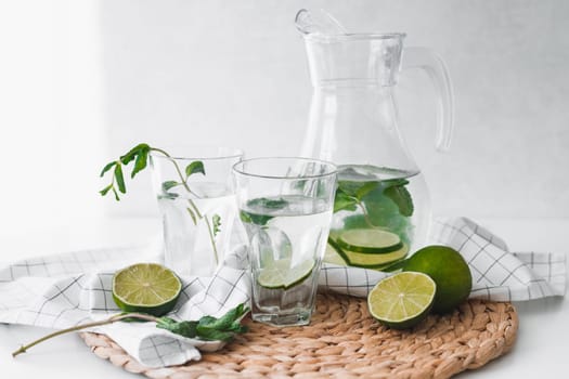 Detox water with lime fruit and mint leaves in jar and glasses.