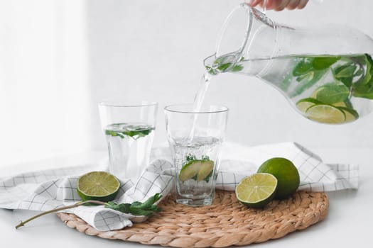 Detox water with lime fruit. Hand pouring lime fruit water from jug into glasses.