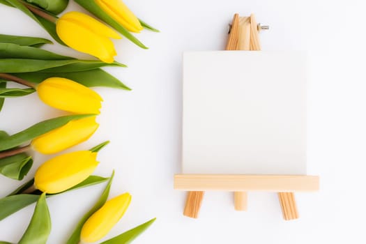 Flat lay with yellow tulip flowers, empty picture frame on white background. Concept for greeting card for Easter, Mother's day, International women's day, Saint Valentine's day. High quality photo