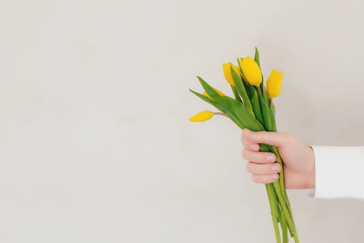 Hand holding bouquet with yellow tulip flowers on gray concrete background. Concept for greeting card for Easter, Mother's day, International women's day, Saint Valentine's day. High quality photo