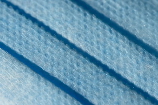 Frame filling abstract background texture of single use folded blue face mask. Individual plastic fibers visible under the high magnification.