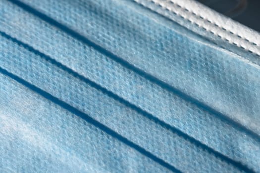 Close up of the front blue surface of a medical or surgical face mask. Man made single use item of Personal protective equipment, plastic texture.