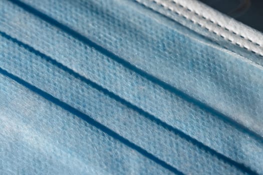 Blue dimpled texture and folds of a disposable 3-ply medical face mask. Mandatory use for many people in public spaces due to Covid aka coronavirus.