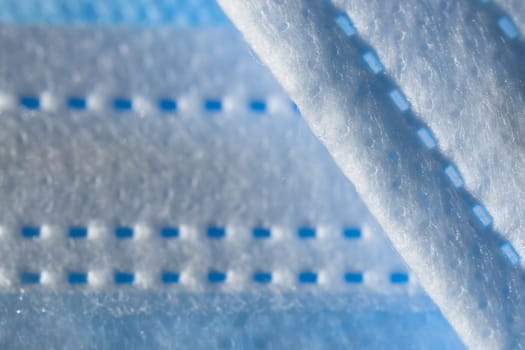 Disposable 3-ply face mask in blue color abstract background. Focus on foreground with plenty of copy space. Micro detail of medical face covering.
