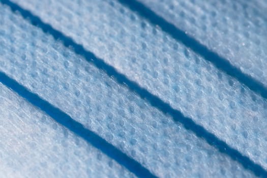 Blue doctors face mask used for coronavirus or covid forms a full frame background texture. Dimpled blue surface and microscopic fiber material detail