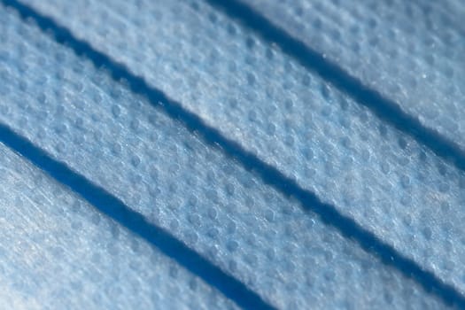 Microscopic magnification of the surface of a medical or surgical style face mask. Blue dimpled plastic texture makes a full frame abstract background