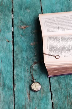 An antique pocket watch and an old book on a blue wooden floor