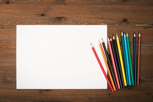 The sheet is pure white and colored pencils for drawing on a wooden background with a place to copy. Mock-up, mockup, layout.
