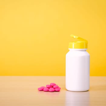 A white jar with scattered red pills on a yellow background. Place for the label, logo, layout.