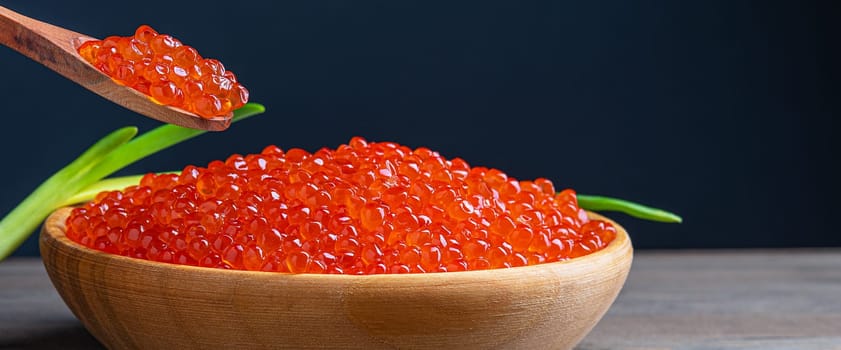 Red caviar in a wooden cup on a wooden background with a spoon. Place for advertisement, logo, label, mockup, mock-up.