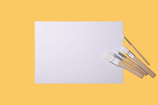 A clean white sheet and paint brushes on a yellow background with a place to copy. Mock-up, mockup, layout.