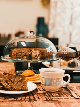 Homemade apple pie in a glass stand on the table a cup of tea, a lemon, a spoon and a cut piece of cake.
