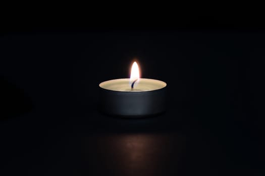A burning candle on a dark background with a flare in the foreground. Layout, mockup.