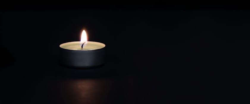 A burning candle on a dark background with a flare in the foreground. Layout, mockup.