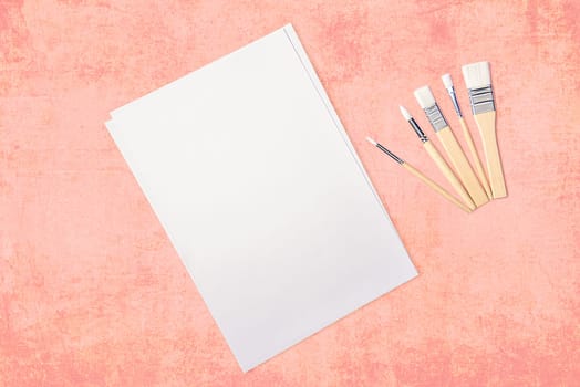 A clean white sheet and brushes on a textured pink background with space to copy. Layout, mockup, layout.