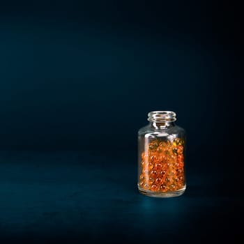 A glass jar with pills of bright orange yellow color on a blue background. Place for the label, logo, layout.