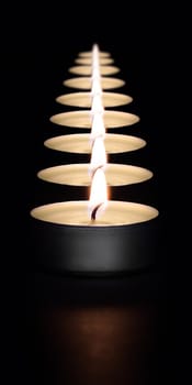 A row of burning candles on a dark background with a flare in the foreground. Layout, mockup.