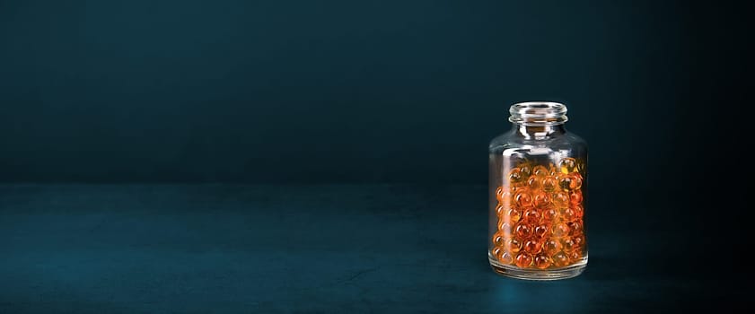A glass jar with pills of bright orange yellow color on a blue background. Place for the label, logo, layout.