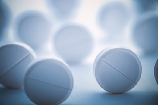 A pile of white pills scattered on a white background with blue tinting. Selective focus. Mockup layout, template.