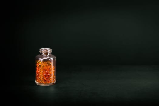 A glass jar with pills of bright orange yellow color on a green background. Place for the label, logo, layout.