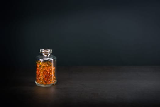 A glass jar with pills of bright orange yellow color on a gray background. Place for the label, logo, layout.