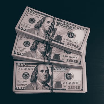 Wads of dollars in cash on a dark table. Three hundred-dollar packs.