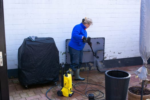 Woman cleaning terrace with a power washer - high water pressure cleaner on wooden terrace surface