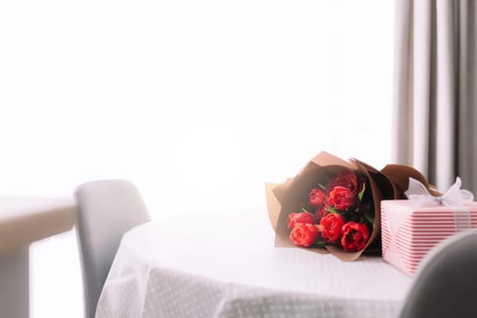 A bouquet of red tulips on the table and pink gift box. Concept for a greeting card. High quality photo