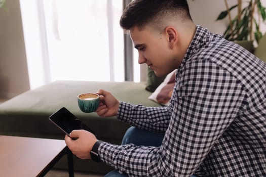 Smiling man holds and reading smartphone with black screen and coffee cup. Blurred background. High quality photo