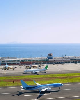 Airplane taking off runway of Madeira International Airport, sunny ocean view in background, Funchal, Portugal