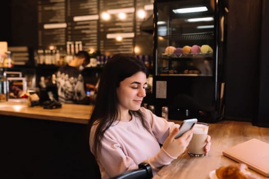 Girl smiling, drinks coffee in cafe and reading phone. Blurred background. High quality photo
