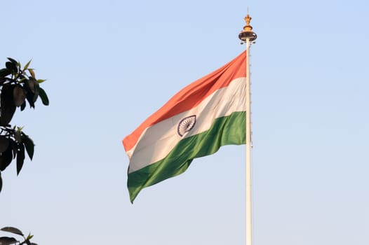 Indian flag flying against blue sky background. The National Flag of India is a horizontal rectangular tricolor (saffron, white and green color) with the Ashoka Chakra at its center.