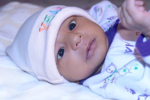 Close up portrait of a cute newborn baby boy lying bed and looking at camera. One month old Sweet infant toddler in winter clothing Closeup. Indian ethnicity. Front face. Child care background