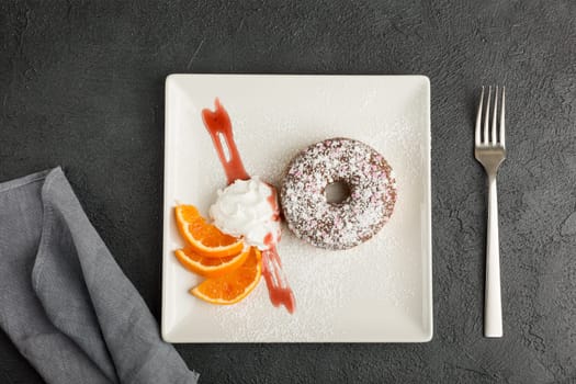 donut decorated with hearts and powdered sugar. Served on a plate decorated with orange slices. Restaurant menu concept. Flat lay. Selective focus.