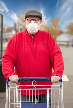 A senior man wears an N95 respirator mask while pushing a shopping cart outside of a grocery store. The man is protecting himself from coronavirus and other airborne particles and diseases.