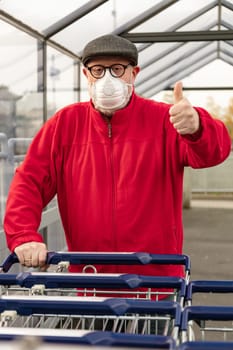 A senior man wears an N95 respirator mask while pushing a shopping cart outside of a grocery store. The man is protecting himself from coronavirus and other airborne particles and diseases.