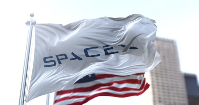 Hawthorne, CA, USA, March 9th 2021: white flag with the SpaceX logo flapping in the wind with the American stars and stripes flag in the background. Aeronautical technology and space missions.