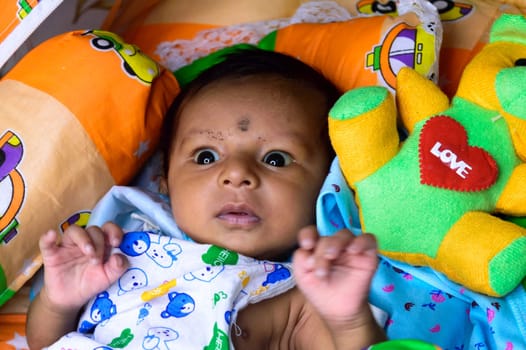 Close up portrait of cute Sweet infant toddler feeling wonder and amazed about surrounding environment. Beautiful Newborn Baby looking something unfamiliar and remarkable astonishingly. Indian ethnicity. High angel Front view.