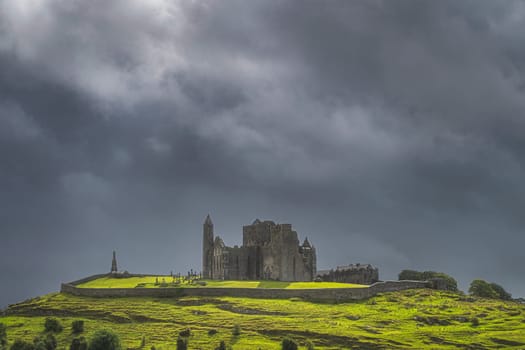 Rock of Cashel castle illuminated by sunlight and surrounded by dramatic dark storm clouds. Known as Cashel of Kings or St. Patricks Rock, Ireland