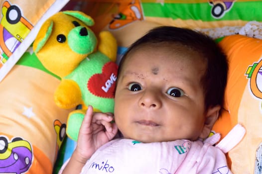 Close up portrait of cute Sweet infant toddler feeling wonder and amazed about surrounding environment. Beautiful Newborn Baby looking something unfamiliar and remarkable astonishingly. Indian ethnicity. High angel Front view.