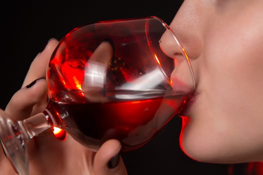 Beautiful girl drinking red wine on black background