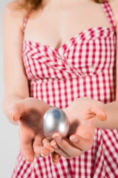 Manicured hands of a young woman in a red shirt holding an egg.