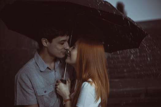 Man and the girl kiss in the rain. Photo contains glare from lights.