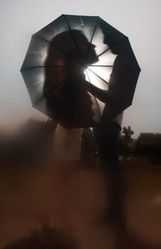 Love in the rain / Silhouette of kissing couple under umbrella