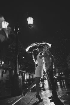 Man and the girl kiss in the rain. Photo contains glare from lights.